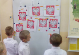 Trzech chłopców podziwia gotowe już prace plastyczne przedstawiające godło Polski